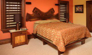 A bed with an orange wall and wooden headboard.